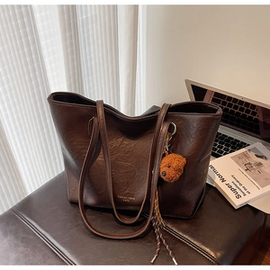 Detail of dark brown tote bag with crumpled leather texture and teddy bear pendant
