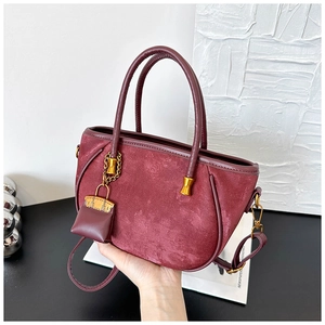 Detail of burgundy velvet handbag with leather handle and gold chain accessory