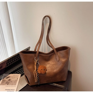 Detail of deep brown faux leather tote bag with a plush charm and woven tassel detail