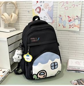Close-up of black backpack featuring a cartoon house pocket design and plush dog charm