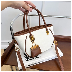 Detail of off-white suede tote bag with brown leather trim and mini bag charm