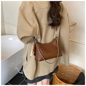 Brown woven crossbody bag with metal chain and ethnic beaded charm detail on a trench coat