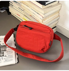 Detail view of red nylon crossbody bag with zipper pockets and adjustable black strap