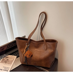 Detail of caramel brown faux leather tote bag with plush bear charm and long shoulder strap
