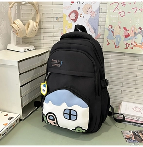 Detail view of black school backpack with blue-white patchwork and a yellow cartoon charm
