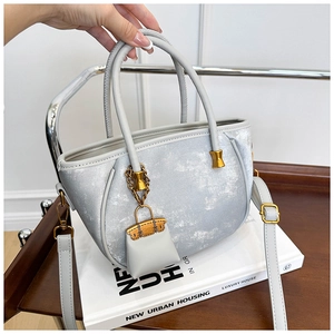 Detail of silver textured bucket bag with gold hardware and mini bag charm accessory