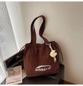 Braune Nylon-Beuteltasche mit weißem BANATU-Aufdruck und gelbem Mond-Plüsch-Anhänger