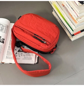 Detailed view of red nylon crossbody bag with dual black zippers and textured finish