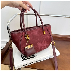 Detail of burgundy suede bucket bag with woven handles and golden mini charm pendant