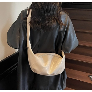 Detail view of the creamy beige croissant bag with a glossy leather finish and knot strap