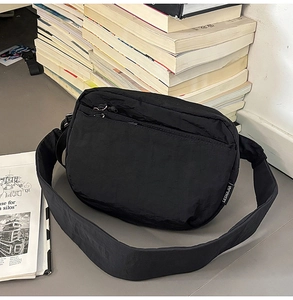 Detail of black nylon crossbody bag with multiple zip compartments on a grey surface