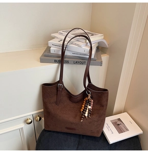 Close-up of brown suede tote bag featuring a colorful beaded charm and silver hardware