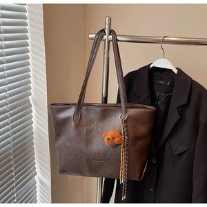 Detail of dark brown leather tote bag showing fine pleated texture and plush bear charm