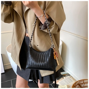 Close-up of black woven leather handbag with metal chain strap and wooden bead charm