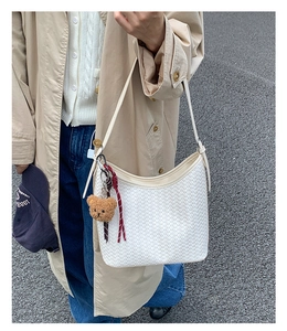 Macro shot of white woven texture shoulder bag with cute bear charm and knotted rope detail