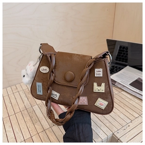 Detalle de bolso bandolera marrón con parches decorativos y colgante de conejo de peluche