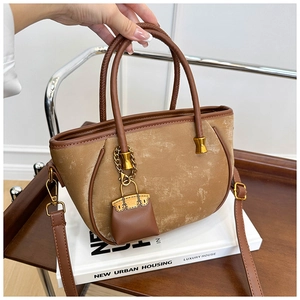 Close-up of vintage camel suede bucket bag with brown leather handles and gold pendant