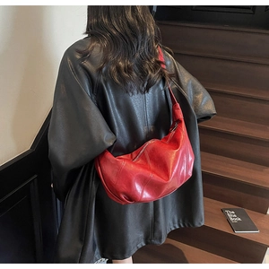Red crescent shoulder bag in textured leather worn with a black coat on wooden stairs
