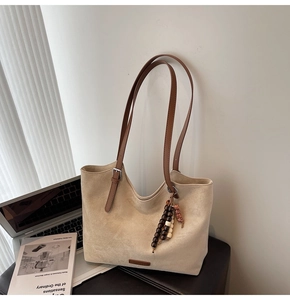 Detail view of beige suede tote bag with brown leather straps and beaded charm