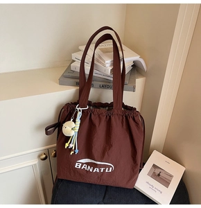 Braune Nylon-Beuteltasche mit weißem Logo und einem gelben Mond-Plüschanhänger-Detail