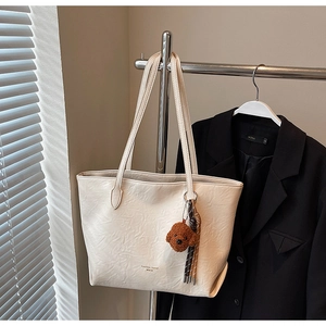 Detail of white textured leather tote bag featuring a cute brown teddy bear charm