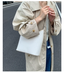 Detail of white woven crossbody bucket bag texture on beige trench coat outfit