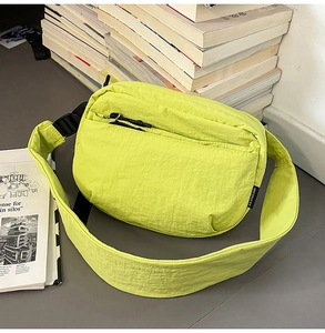 Macro shot of neon yellow nylon crossbody bag on books showing pleated texture and zippers