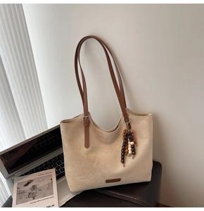 Detail of minimalist suede tote bag with brown adjustable handles and wooden bead pendant