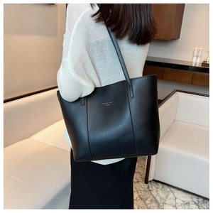 Détail du grand sac cabas noir avec lettrage doré porté à l'épaule sur un mannequin