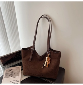 Detail of dark brown suede tote bag featuring a bohemian beaded charm and slim strap