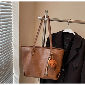Detail of brown litchi pattern tote bag with leather strap and cute dog plush charm