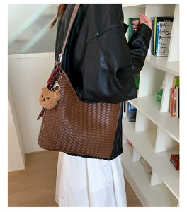 Close-up of brown woven bucket bag with teddy bear charm and stylish checkered scarf