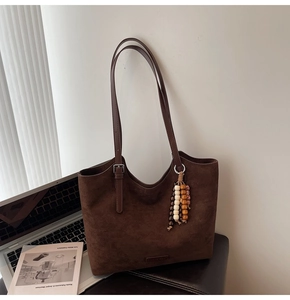Detailed macro view of dark brown suede tote bag with double straps and wooden bead charm