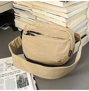 Detail of nylon crossbody bag with zipper pocket and brand tag on textured surface