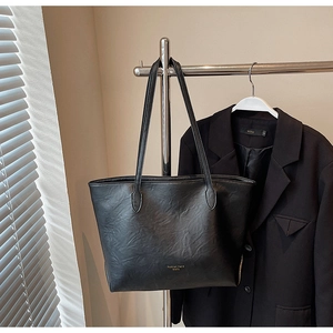Detail of black faux leather tote bag featuring a textured finish and golden logo