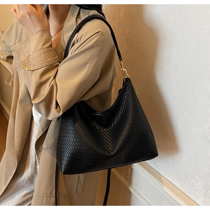 Détail du sac fourre-tout noir en cuir tressé avec boucle dorée porté à l'épaule