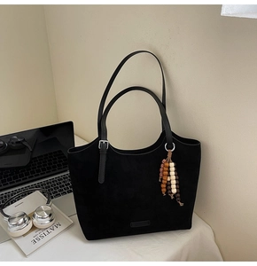 Close-up of black suede tote bag with ethnic wooden beads and embossed logo detail