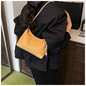 Detail of woven leather crossbody bag with chain strap and ethnic charm on back of jacket