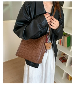 Detail of a brown woven leather hobo bag featuring a cute plush bear charm accessory
