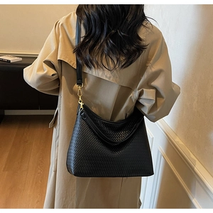 Détail de la texture tressée du sac cabas noir avec boucles dorées porté sur un trench