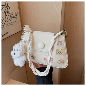 Detalle de bolso crema con correa tejida, parches y colgante de perrito de felpa