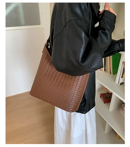 Close-up of brown woven leather tote bag with adjustable shoulder strap on model
