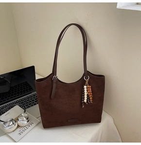 Detail of dark brown faux suede tote bag with wooden bead charm and minimalist logo plate