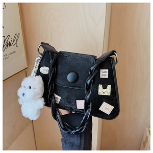 Detalle del bolso tipo cubo de ante negro con parches de dibujos y perro peluche