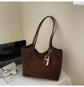 Detail view of dark brown suede tote bag with wooden bead tassel on a desktop scene
