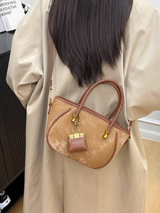 Khaki suede bucket bag with leather handles and mini charm shown on a trench coat model