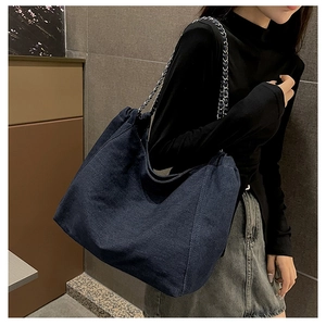Detail of blue denim tote bag with silver chain strap shown on model shoulder