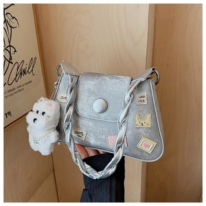 Bolso bandolera plateado con asa trenzada, parches y detalle de charm de perrito de peluche