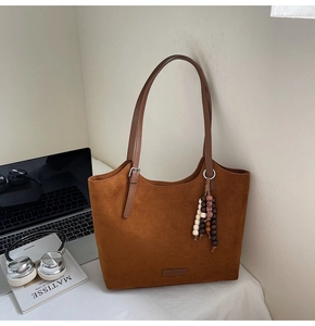 Close-up of brown suede tote bag with bohemian bead charm and leather brand tag
