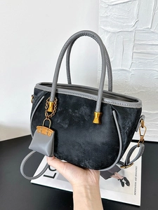 Dark suede bucket bag with grey round handles and a mini bag charm accessory